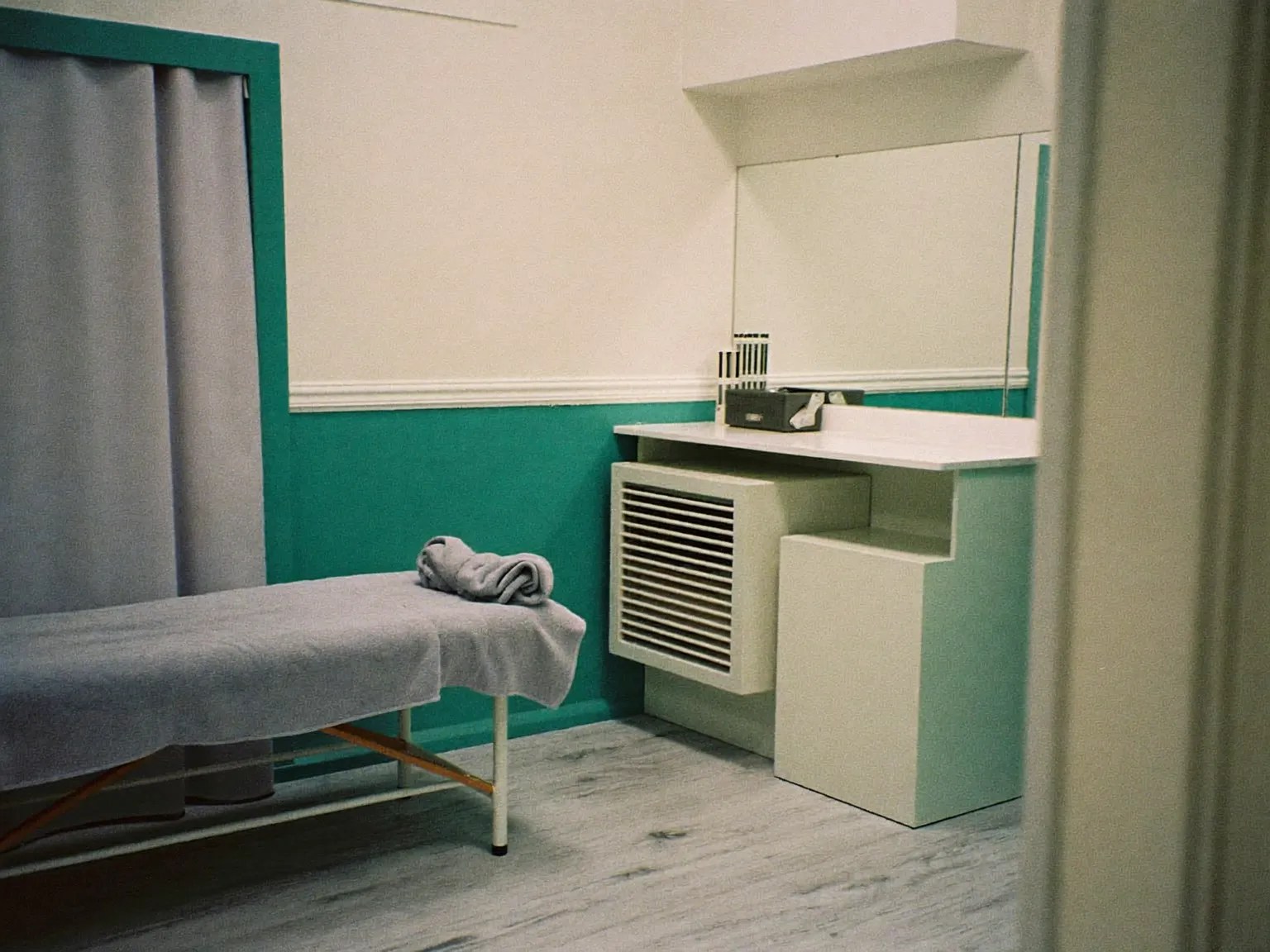 A corner of the treatment room, with the end of the couch, a mirror over a low counter and a curtained doorway