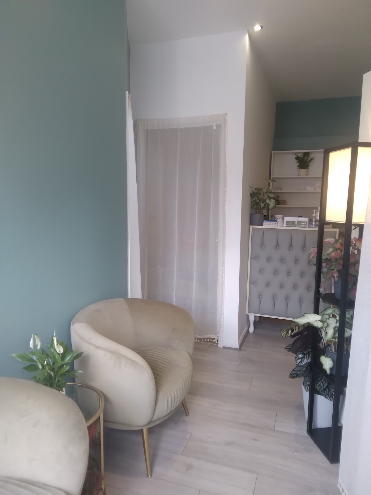 The waiting area at Chic Studio, with a cream tub chair, a small plant and teal and white walls leading to the reception counter